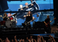 Foo Fighters live im Olympiastadion Berlin mit Sänger, Schlagzeuger und Bassist vor einer großen Gitarrenprojektion.