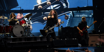 Foo Fighters live im Olympiastadion Berlin mit Sänger, Schlagzeuger und Bassist vor einer großen Gitarrenprojektion.