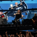 Foo Fighters live im Olympiastadion Berlin mit Sänger, Schlagzeuger und Bassist vor einer großen Gitarrenprojektion.