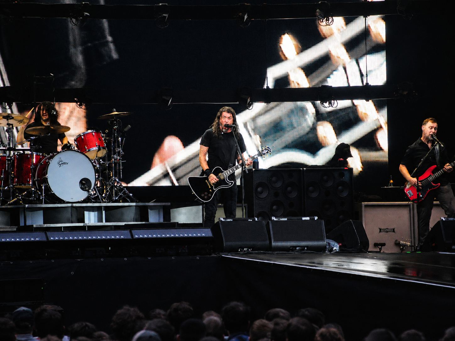 Foo Fighters mit Sänger, Schlagzeuger und Bassist vor einer großformatigen Gitarrenprojektion auf der LED-Wand.