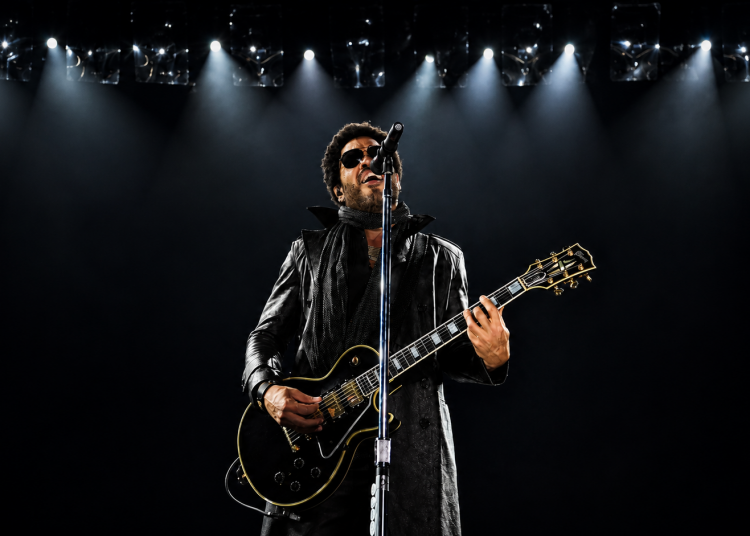 Lenny Kravitz mit schwarzer Gitarre und Sonnenbrille bei einem Konzert unter hellem Bühnenlicht