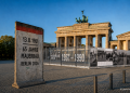 KI-generierte Illustration zu 65 Jahre Mauerbau Berlin 2026 mit Brandenburger Tor, Mauer-Element und Ausstellung zur deutschen Teilung