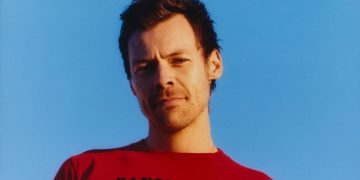 Harry Styles im roten T-Shirt vor blauem Hintergrund