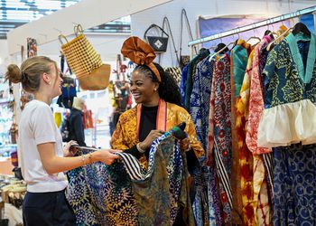 Zwei Frauen betrachten farbenfrohe Kleidung und handgefertigte Textilien an einem Verkaufsstand auf dem Bazaar Berlin.