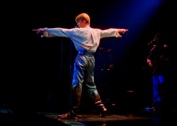 David Bowie steht mit ausgestreckten Armen auf einer dunkel beleuchteten Konzertbühne – Pressefoto zur Show STAGE in Berlin 2027