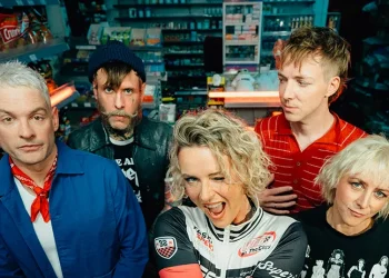 Jennifer Rostock auf einem aktuellen Bandfoto von 2026: Die fünf Musiker stehen gemeinsam in einem Kiosk. Am 8. Mai 2027 spielt die Band im Velodrom Berlin.