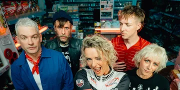 Jennifer Rostock auf einem aktuellen Bandfoto von 2026: Die fünf Musiker stehen gemeinsam in einem Kiosk. Am 8. Mai 2027 spielt die Band im Velodrom Berlin.