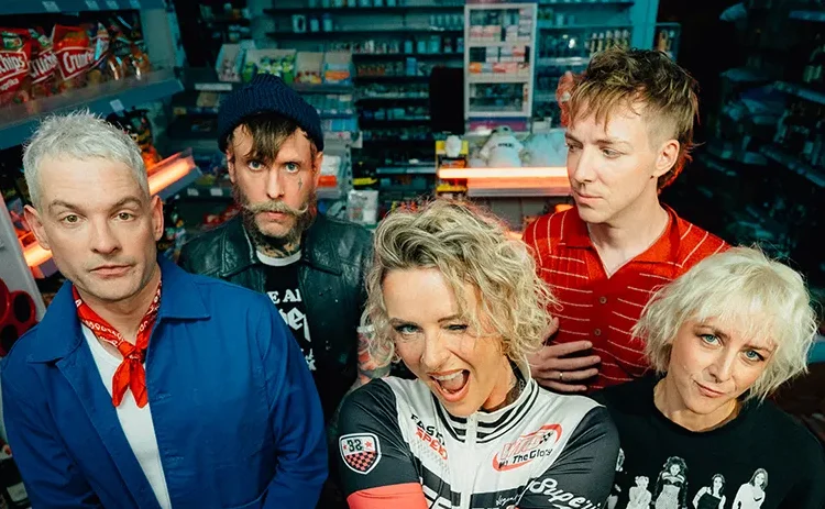Jennifer Rostock auf einem aktuellen Bandfoto von 2026: Die fünf Musiker stehen gemeinsam in einem Kiosk. Am 8. Mai 2027 spielt die Band im Velodrom Berlin.