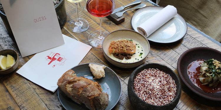 Kreative Sharing-Gerichte, Wein und die Speisekarte des QUI31 auf einem gedeckten Restauranttisch in Berlin-Charlottenburg.