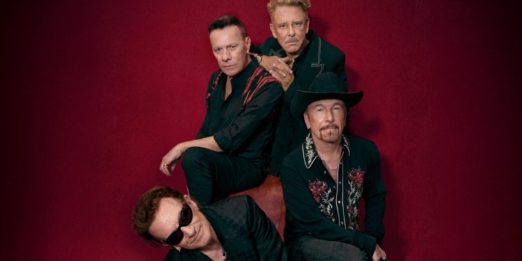 Die vier Mitglieder von U2 auf einem Pressefoto vor dunkelrotem Hintergrund zur Welttournee 2027 mit Konzert im Olympiastadion Berlin.
