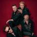 Die vier Mitglieder von U2 auf einem Pressefoto vor dunkelrotem Hintergrund zur Welttournee 2027 mit Konzert im Olympiastadion Berlin.